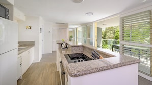 A modern kitchen with granite countertops, a built-in stove, and a dining area with a view of greenery. - 2 Hastings Street (Noosa Heads)