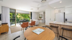 A modern kitchen with white cabinets, a refrigerator, and a dining area with a wooden table and chairs. - 2 Hastings Street (Noosa Heads)