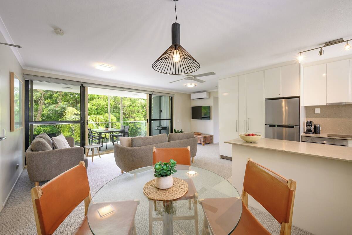 A modern kitchen with a central island, a dining area with a glass table, and a seating area with a sofa and chairs.