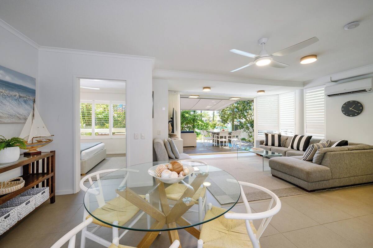 A modern living room with a glass dining table, a sofa, and a ceiling fan.