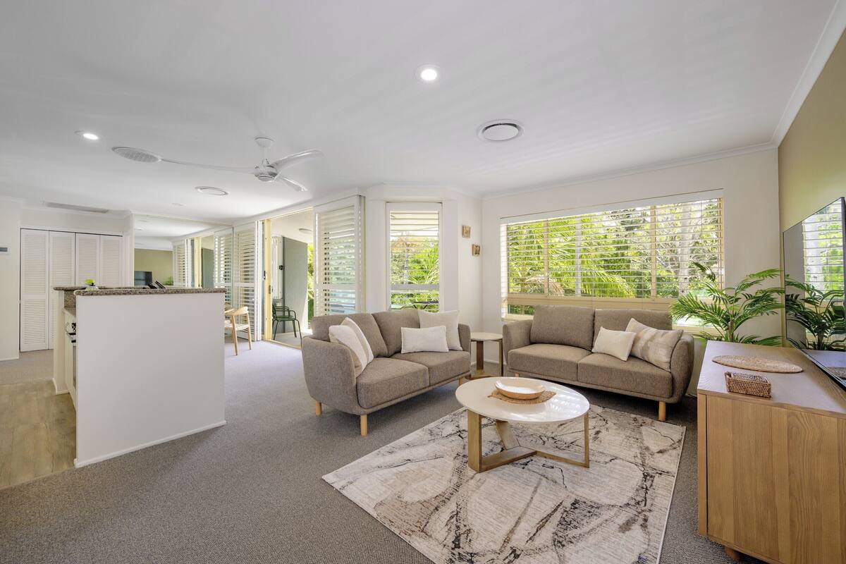 A spacious living area with a sofa set, a coffee table, and a view of greenery outside.