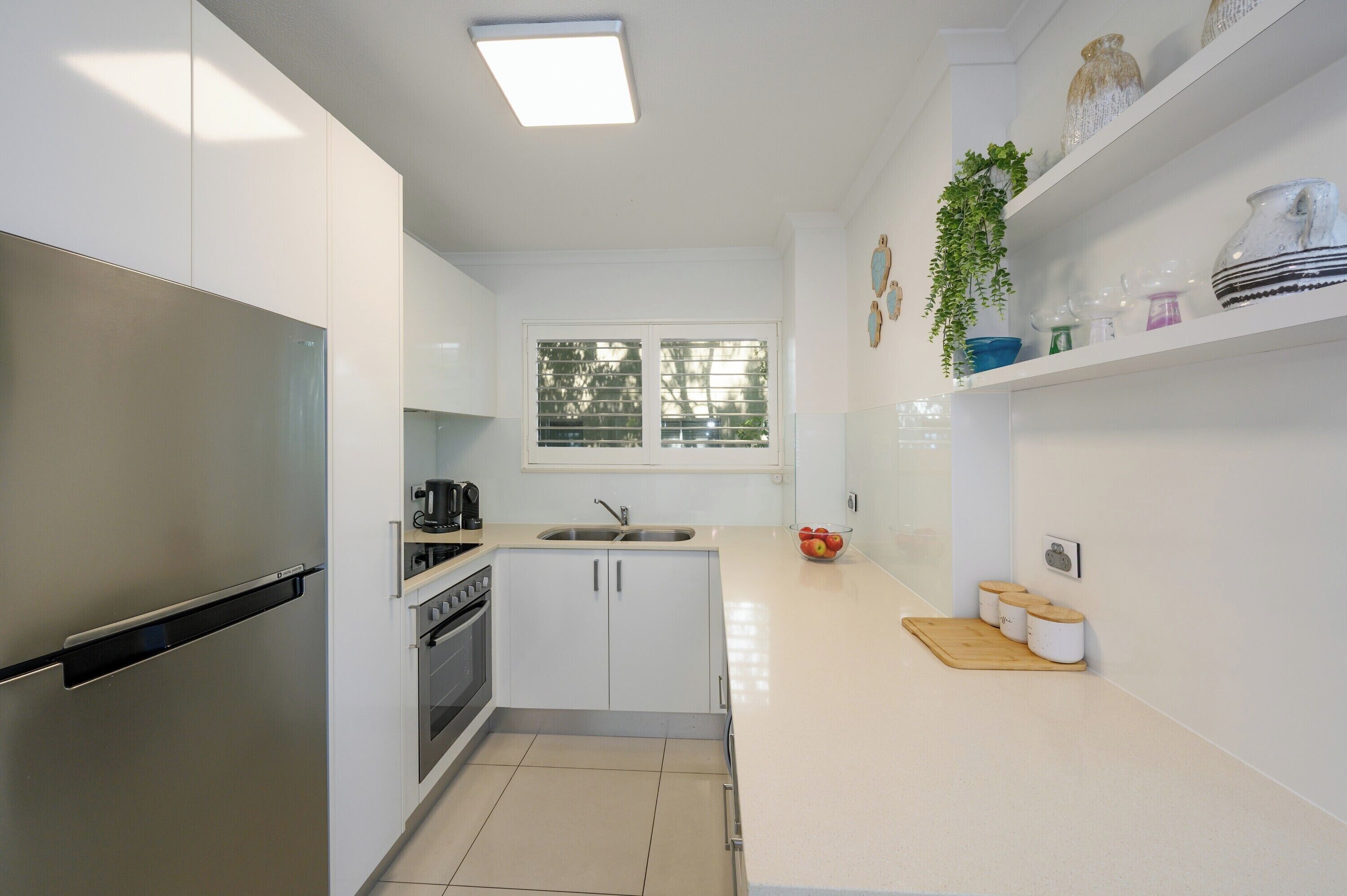Una cocina moderna con armarios blancos, un refrigerador de acero inoxidable, una ventana y una encimera con utensilios de cocina.