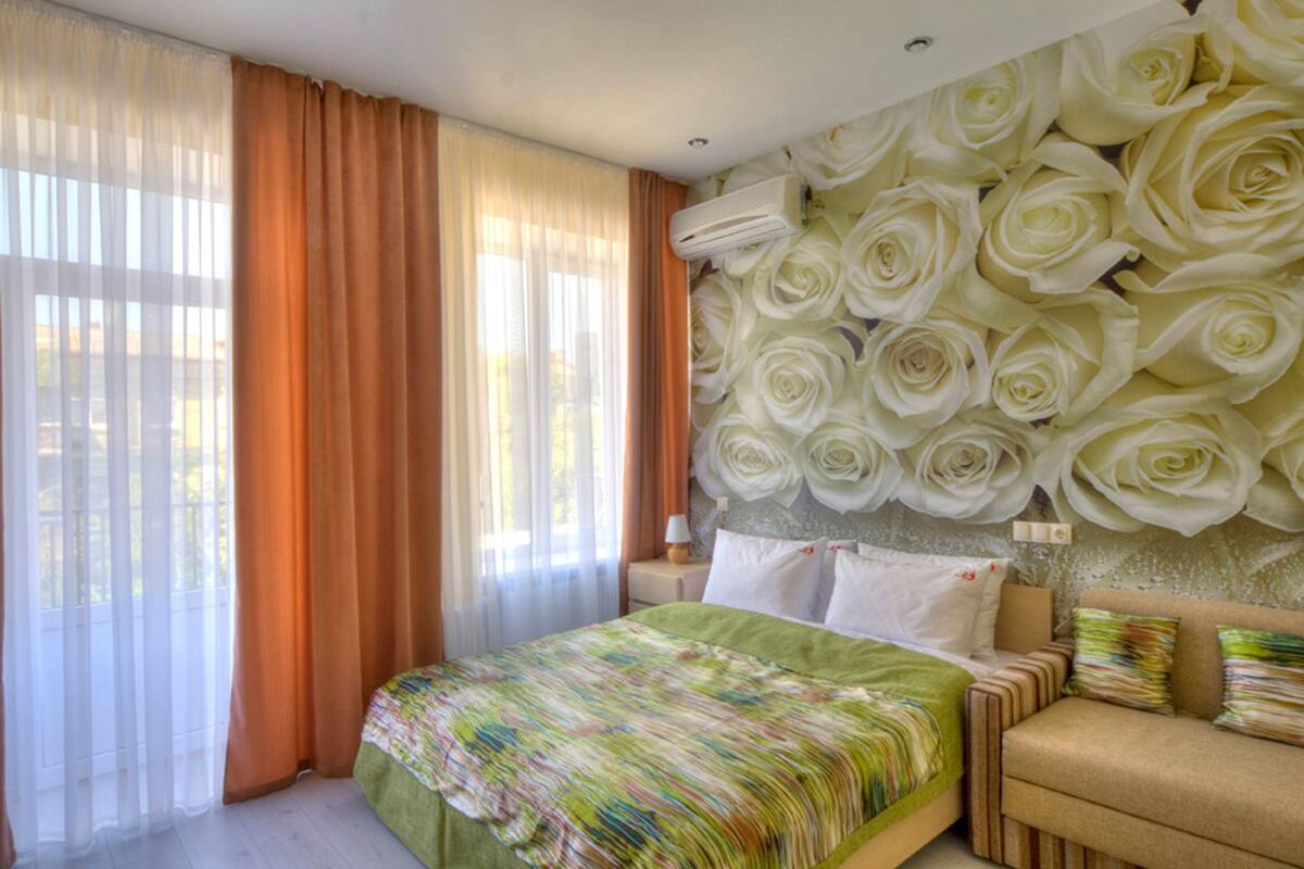 A bedroom with a bed, a sofa, and a wall decorated with large white roses.