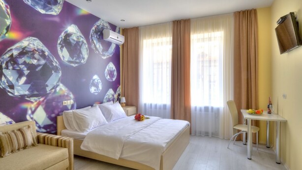A hotel room with a bed, a sofa, a small table with a chair, and a wall with a diamond pattern. - Fire Inn (Kyiv)