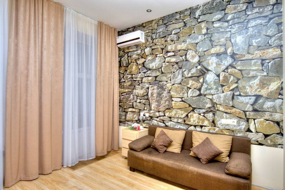 A room with a stone wall, a brown sofa with cushions, and a wooden floor.