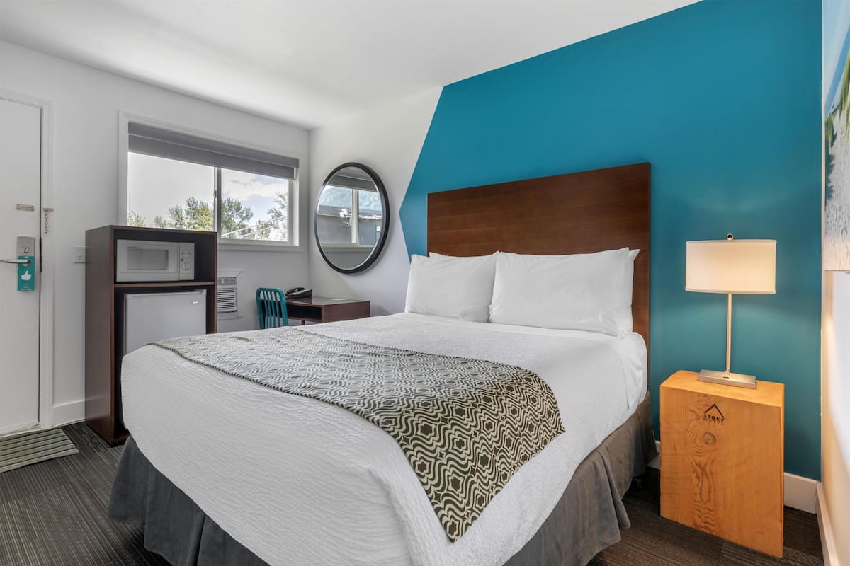 Ein Hotelzimmer mit einem Bett, einem Schreibtisch mit Computer, einer Mikrowelle und einem Fenster.