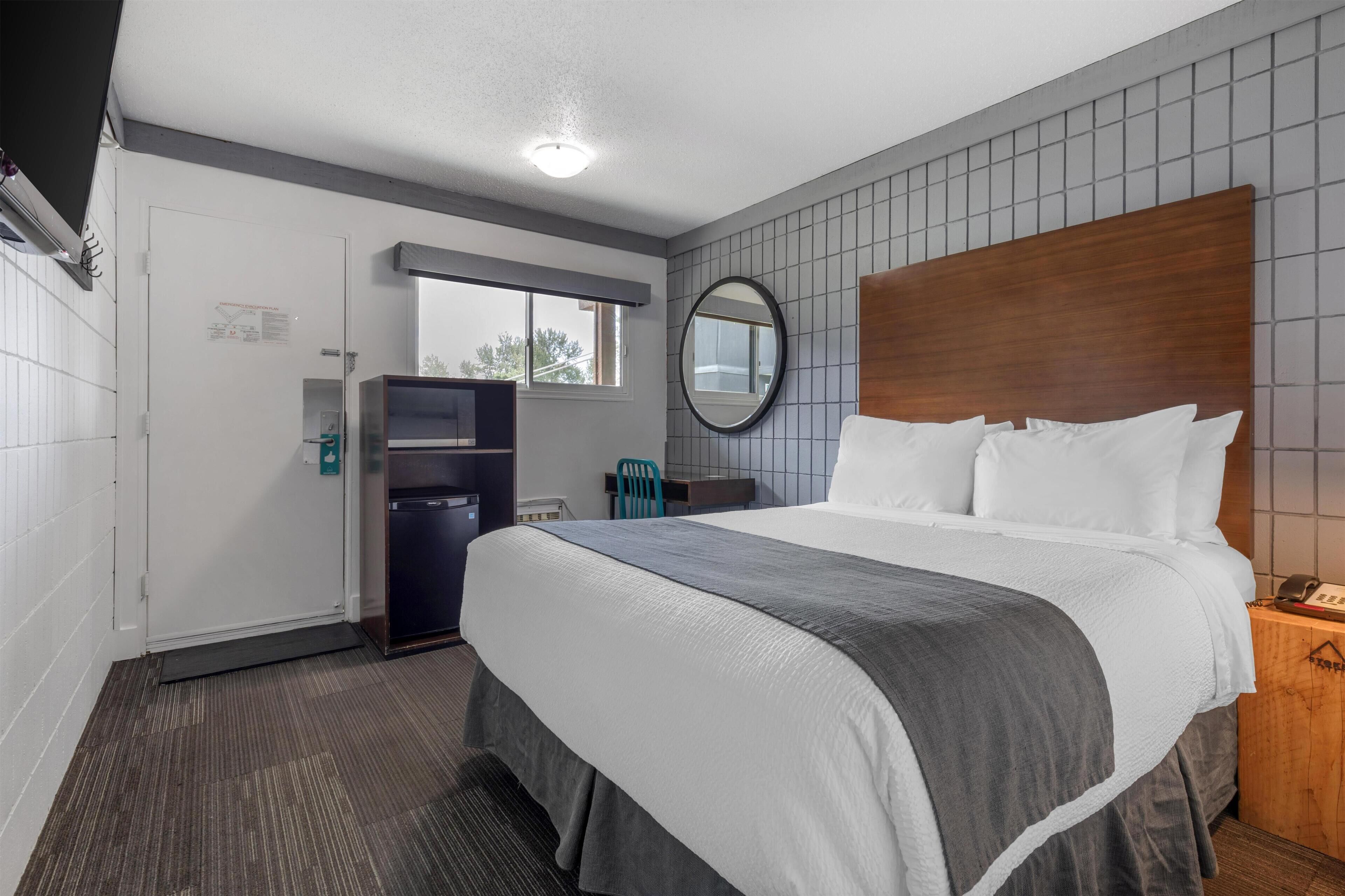 Habitación de hotel con una cama grande, cabecero de madera, escritorio con silla, un refrigerador pequeño y una ventana.