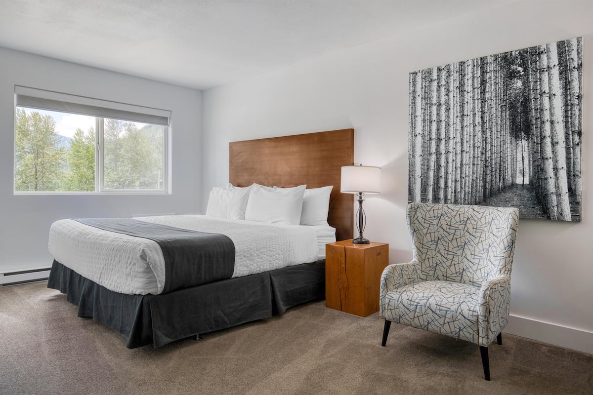 Ein Schlafzimmer mit Bett, Nachttisch, Stuhl, Fenster und Wandbild.