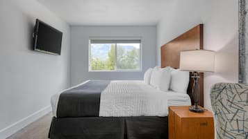 Habitación de hotel con una cama, televisión montada en la pared, ventana con vistas a la montaña, lámpara de noche y sillón estampado.