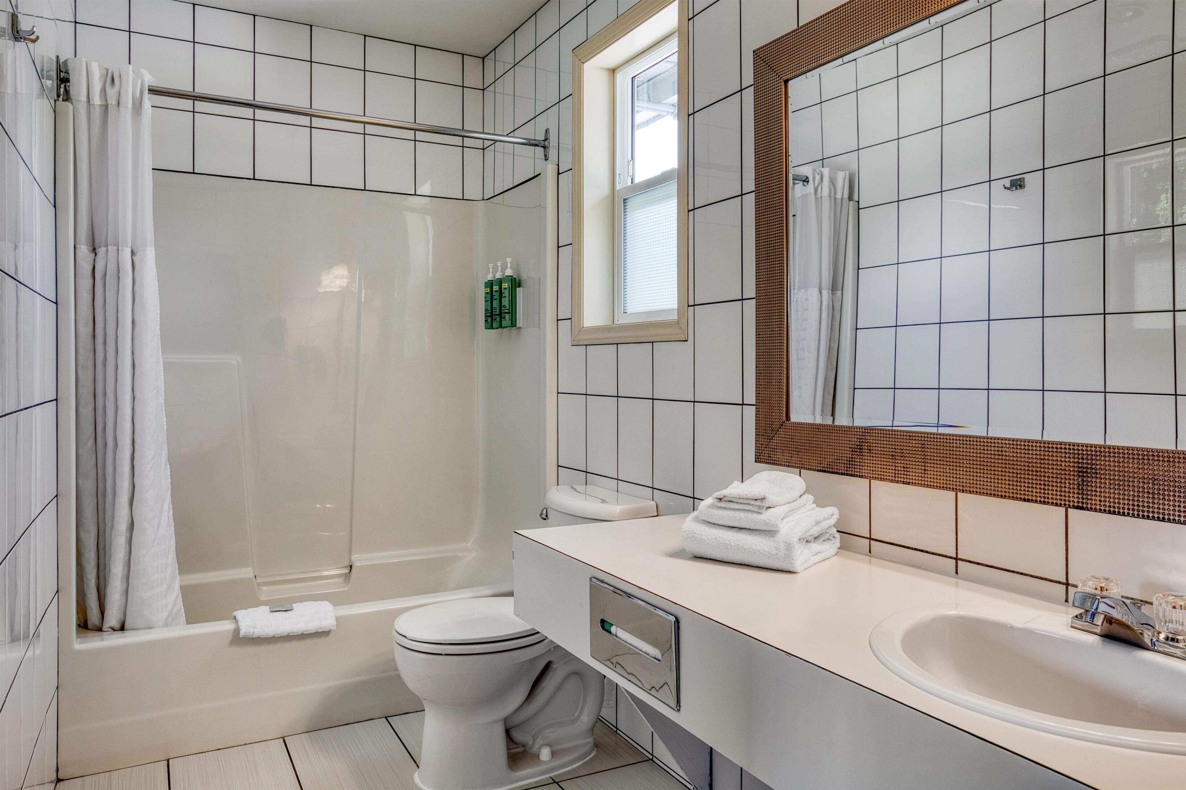 Casa de banho moderna com banheira, sanita e lavatório, com azulejos brancos e um espelho grande.
