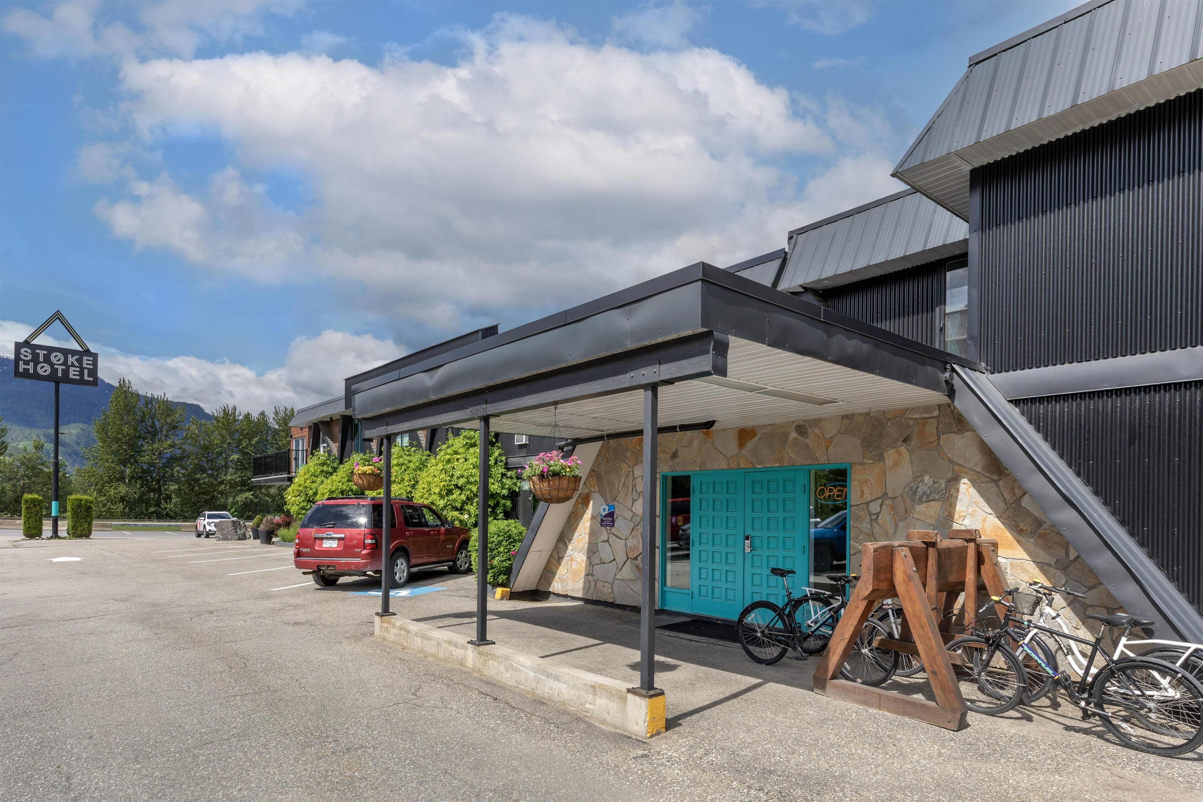Ein Hotel Eingangsbereich mit überdachter Wartezone, einer blauen Tür und draußen abgestellten Fahrrädern.