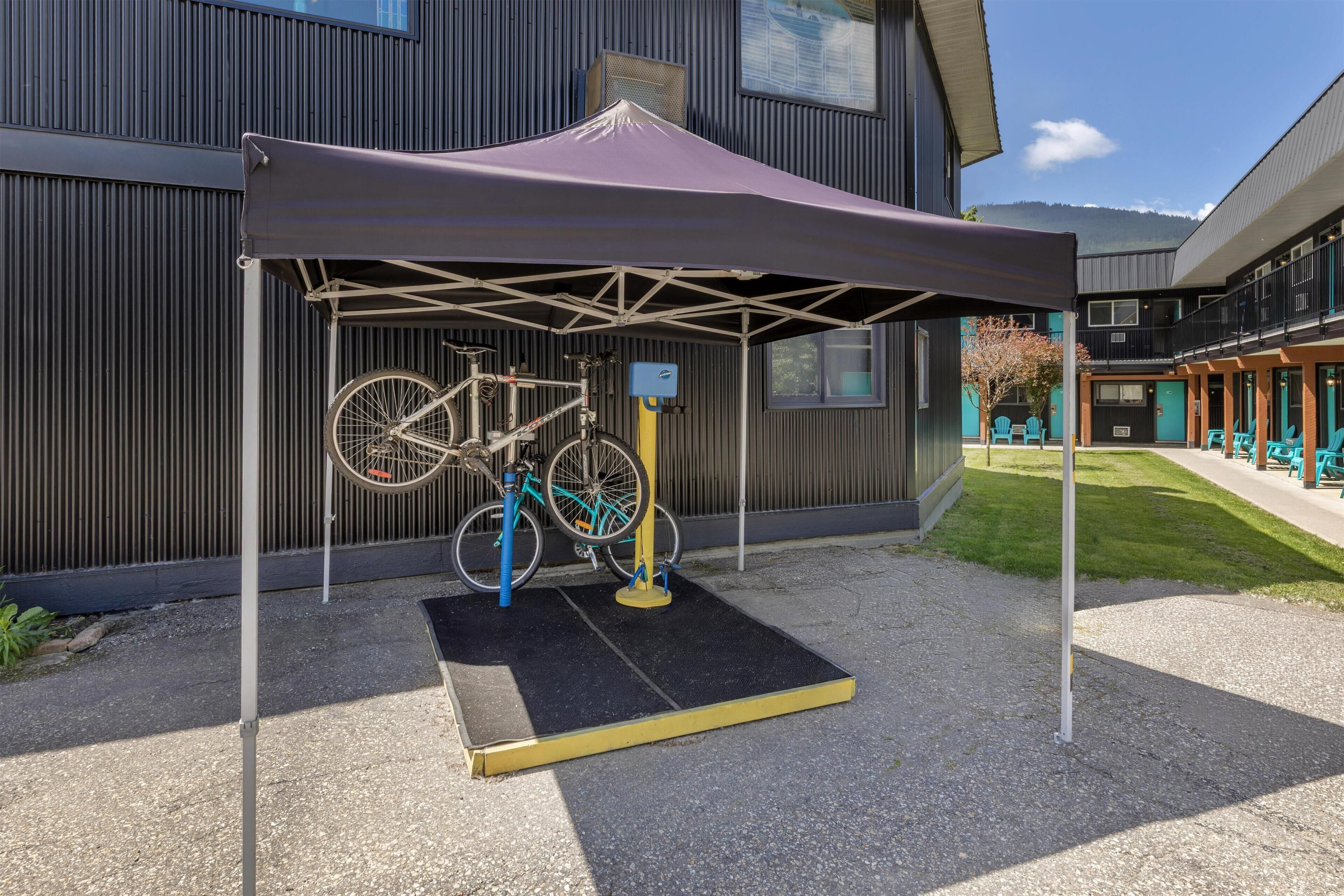 A bicycle under a canopy, a building with a metal exterior, and a grassy area with outdoor seating.