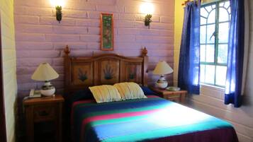 Una habitación con una cama, dos lámparas de noche, un teléfono y un ventanal con cortinas.