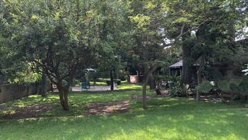 A lush garden with a variety of trees, a paved walkway, and a rustic outdoor seating area.