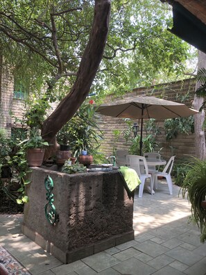 A patio area with a stone planter, white plastic chairs, and an umbrella. - Casa del Retoño (Tlaquepaque)