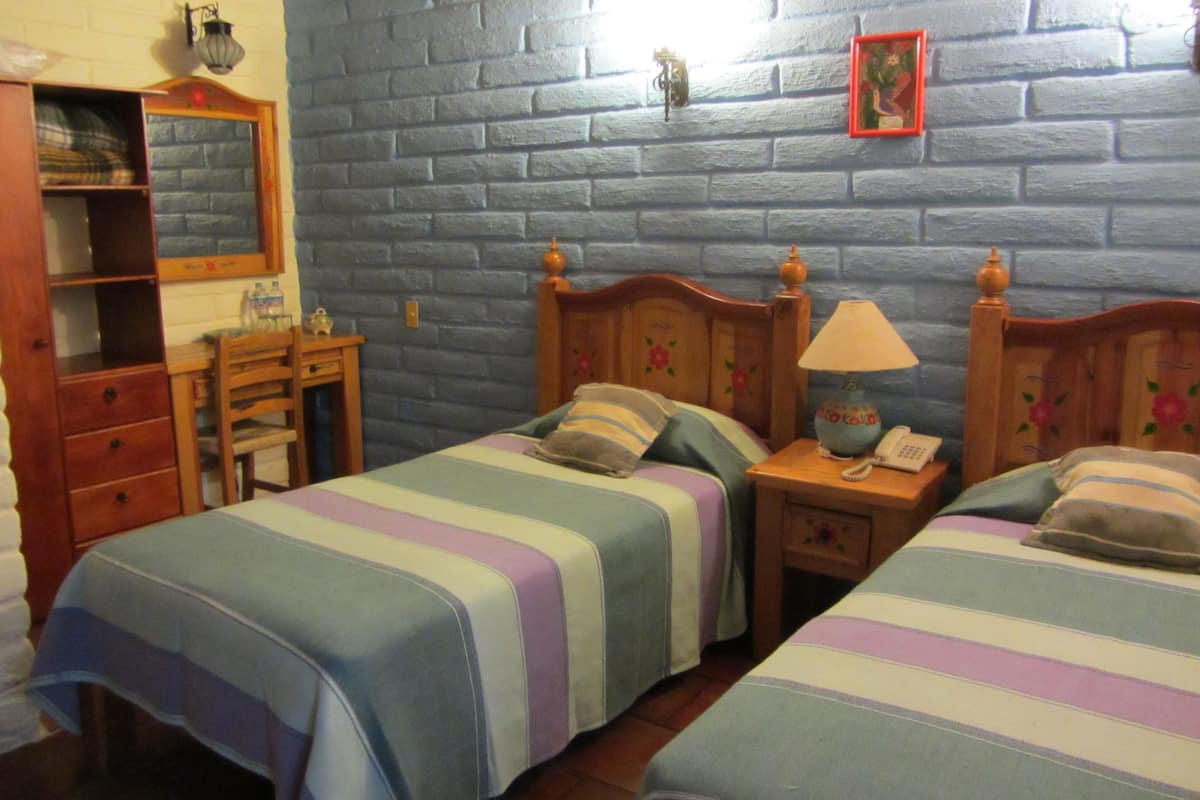 Una habitación con dos camas, un aparador de madera, una mesita de noche con una lámpara y un teléfono instalado en la pared.