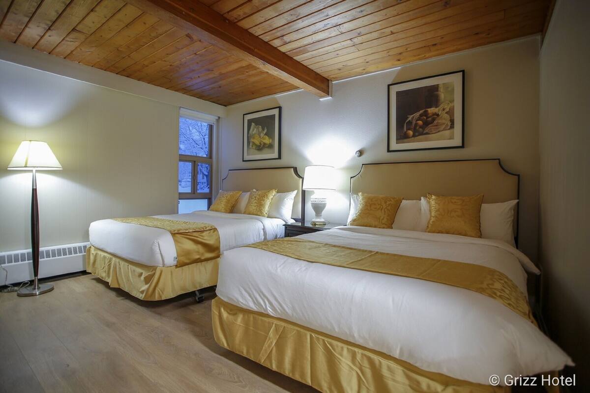 A hotel room with two beds, wooden ceiling beams, and framed artwork on the walls.