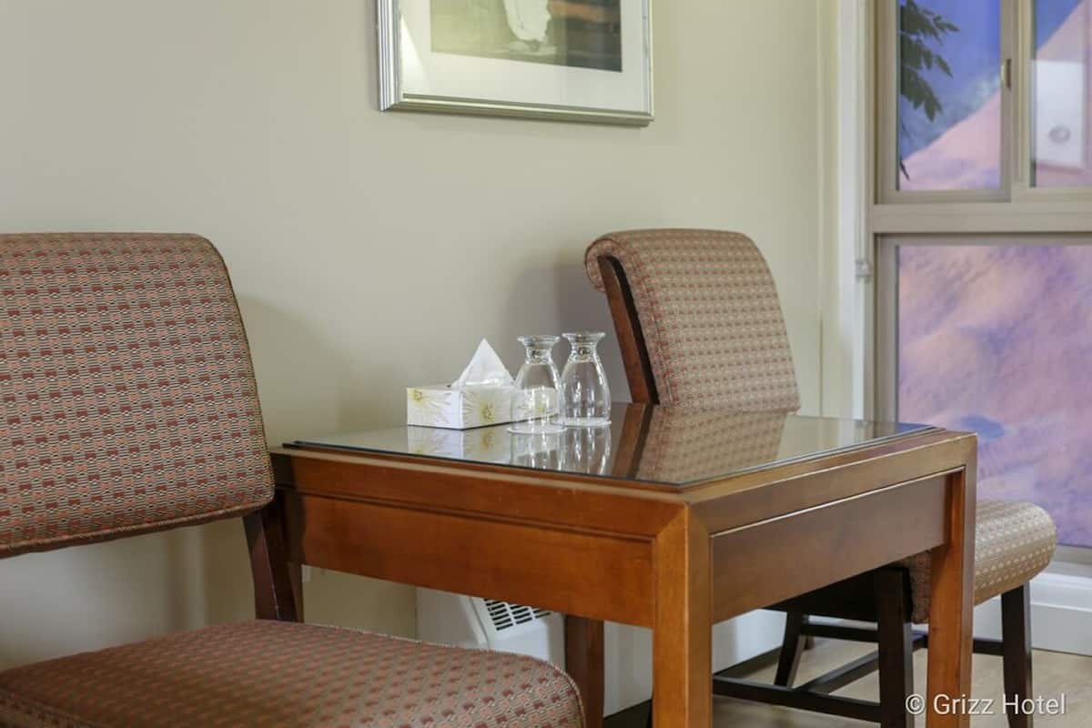 A dining area with a wooden table and patterned chairs, a framed picture on the wall, and a window with a view.