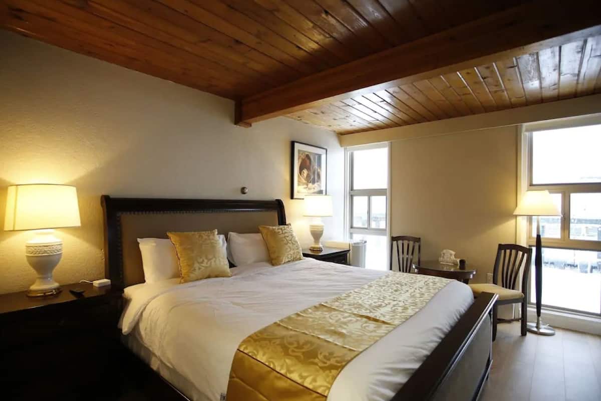 A hotel room with a large bed, two bedside tables with lamps, a wooden ceiling, and a window providing a view.