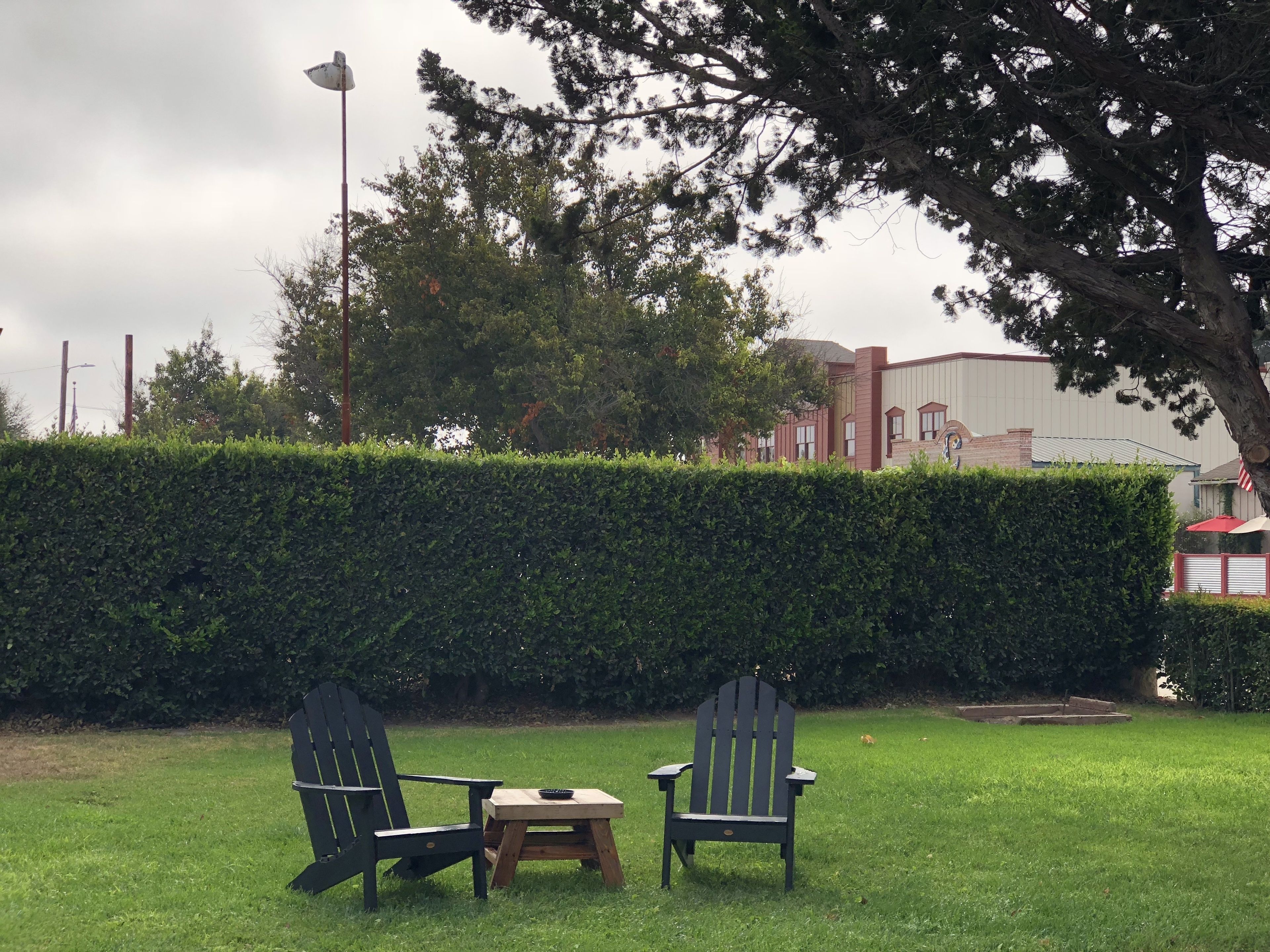 Un espacio al aire libre con césped, dos sillas Adirondack y una pequeña mesa de madera.