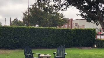 Un espacio al aire libre con césped, dos sillas Adirondack y una pequeña mesa de madera.