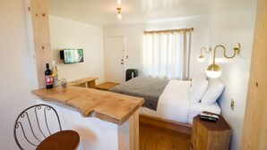 A compact room with a bed, a wooden desk, a chair, a television, and a bedside table with a lamp. - Alamo Motel (Los Alamos)