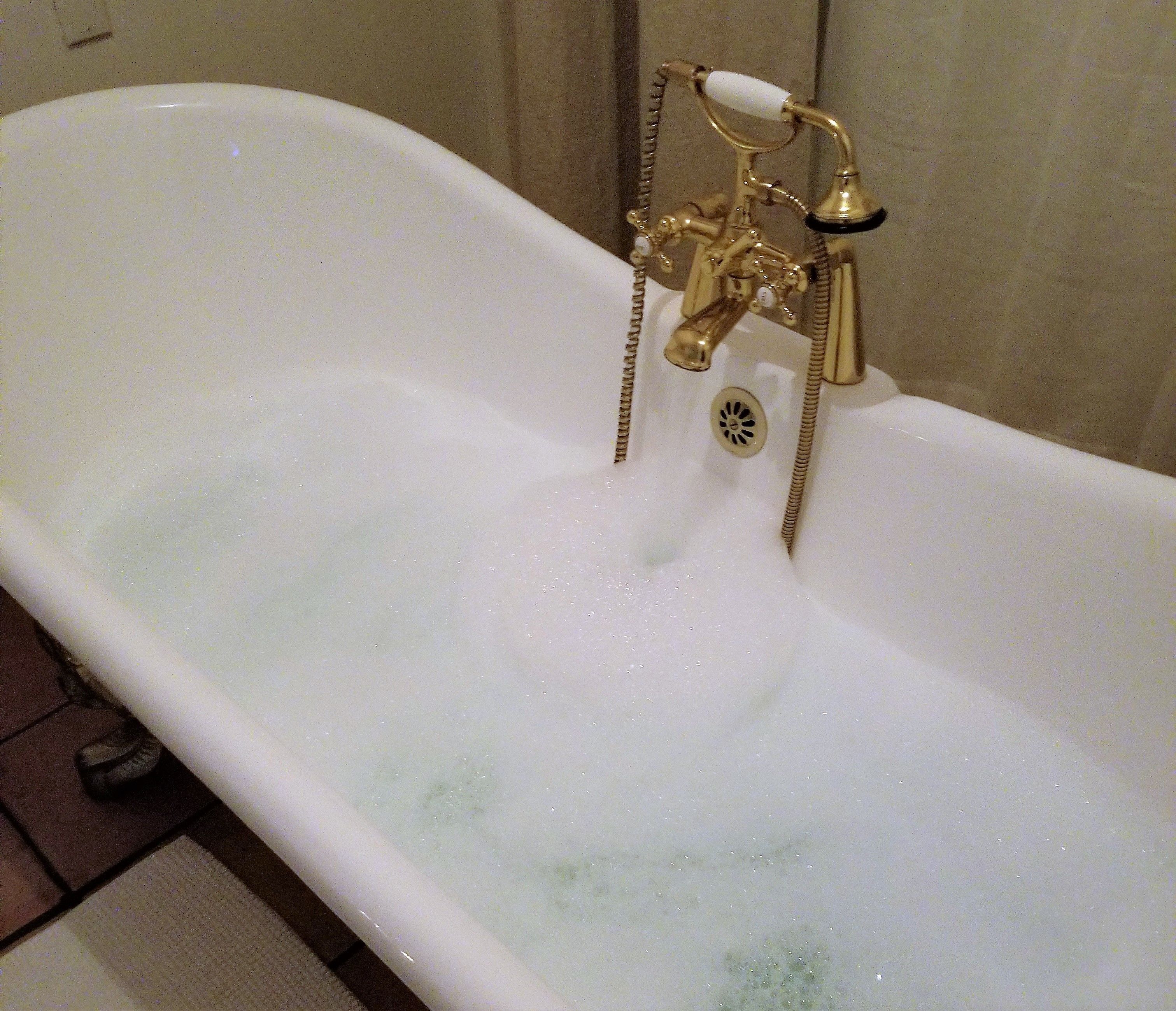 A bathtub with a gold faucet and a drain.