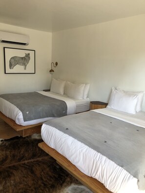 A bedroom with two beds, a mounted air conditioner, a wall-mounted light fixture, and a framed animal print on the wall.