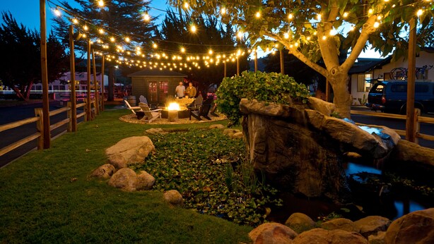 An outdoor seating area with string lights, a fire pit, and a pond. - Alamo Motel (Los Alamos)