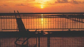A sunset view from a balcony with a metal railing, a chair, and a table. - Riviera Suites (Kanayannur)