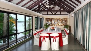 A dining area with a long table set for six, large windows, and a view of the water. - Riviera Suites (Kanayannur)