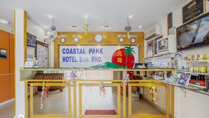 Zona de recepción de hotel con un cartel grande del Hotel Parque Costero, un mostrador de recepción, un área de estar con un sofá y una exhibición de servicios.