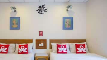 A hotel room with two beds, each with white bedding and red pillows with a white flower design. There are two wall-mounted light fixtures, a small wooden table, and two framed artworks on the walls.