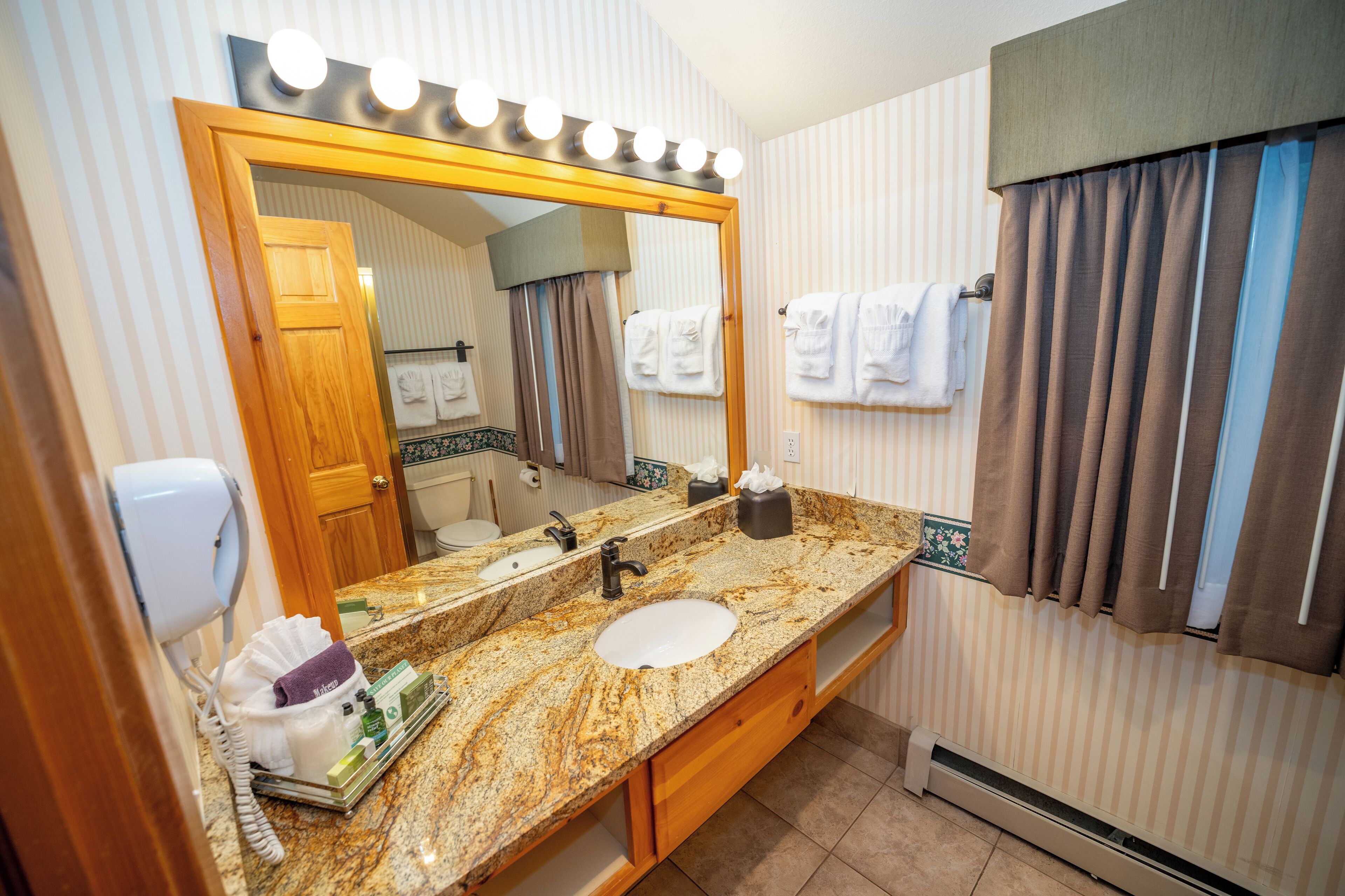 Une salle de bain avec un grand miroir, un meuble-lavabo avec un évier, un porte-serviettes et un sèche-cheveux.