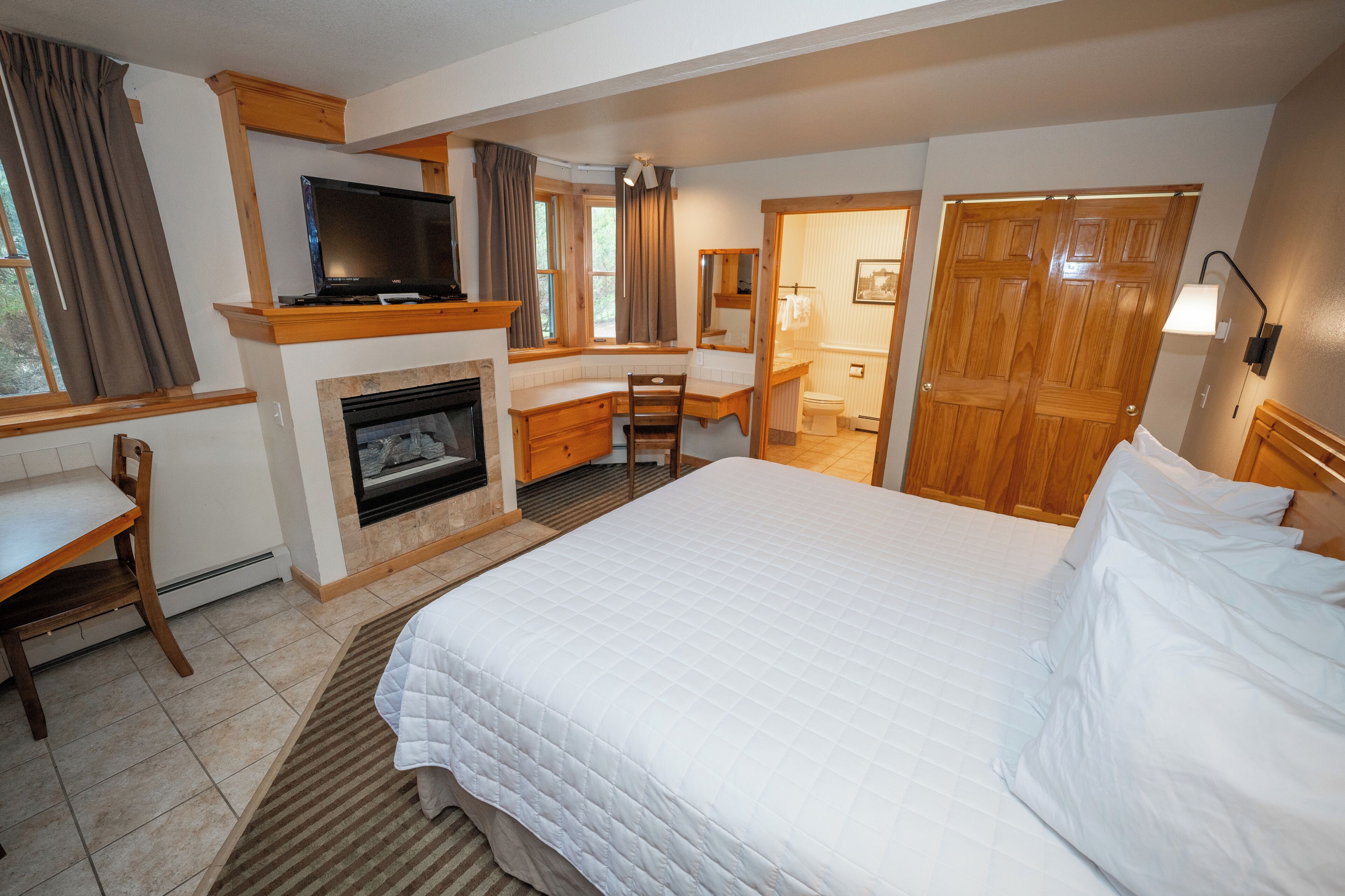 Habitación de hotel con una cama grande, un escritorio con una silla, chimenea, televisión y una puerta de madera.