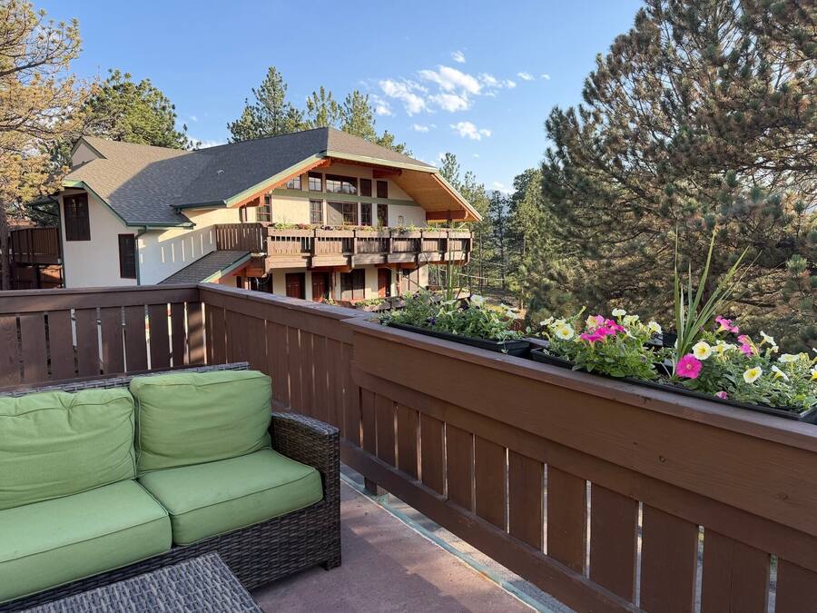 Un balcon agrémenté d’un canapé en osier, d’une clôture en bois et d’un parterre fleuri où poussent différentes plantes.