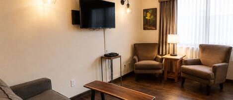 Una sala de estar con un sofá, dos sillones, una mesita de centro, un televisor de pantalla plana y una lámpara.
