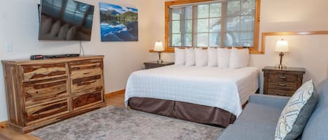 A bedroom with a bed, a wooden dresser, a gray sofa, and two bedside tables with lamps.