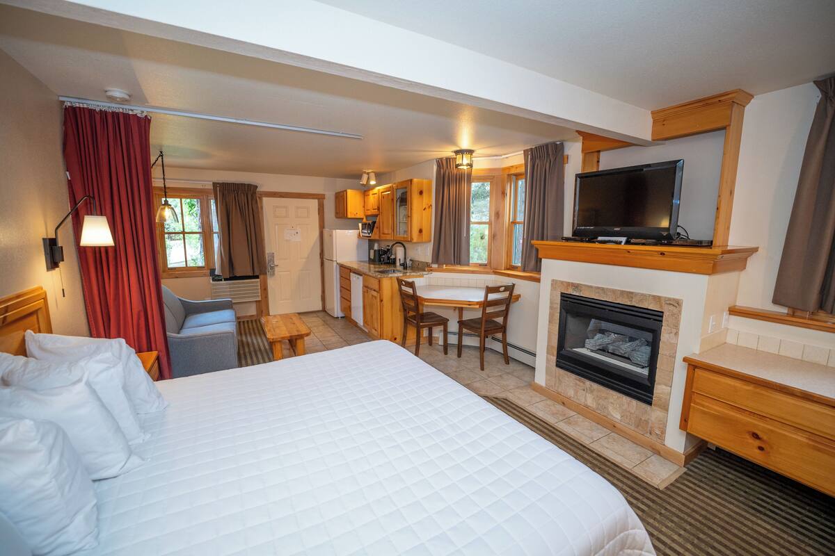 Quarto de hotel com uma cama grande, uma escrivaninha, lareira, televisão e uma kitchenette.