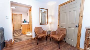 Habitación de hotel con piso de madera, dos sillones de cuero, una mesita redonda, una lámpara y una puerta con espejo.