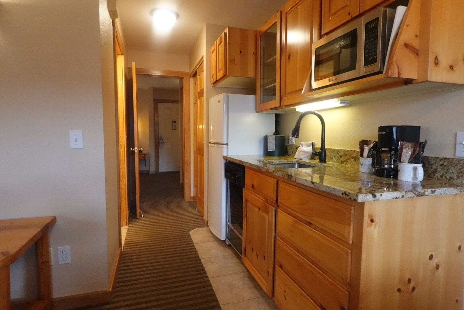 A kitchen with wooden cabinets, a microwave, a coffee maker, and a sink.