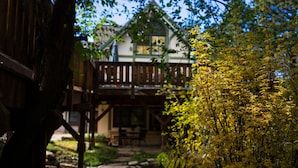 A wooden house with a balcony, surrounded by greenery.