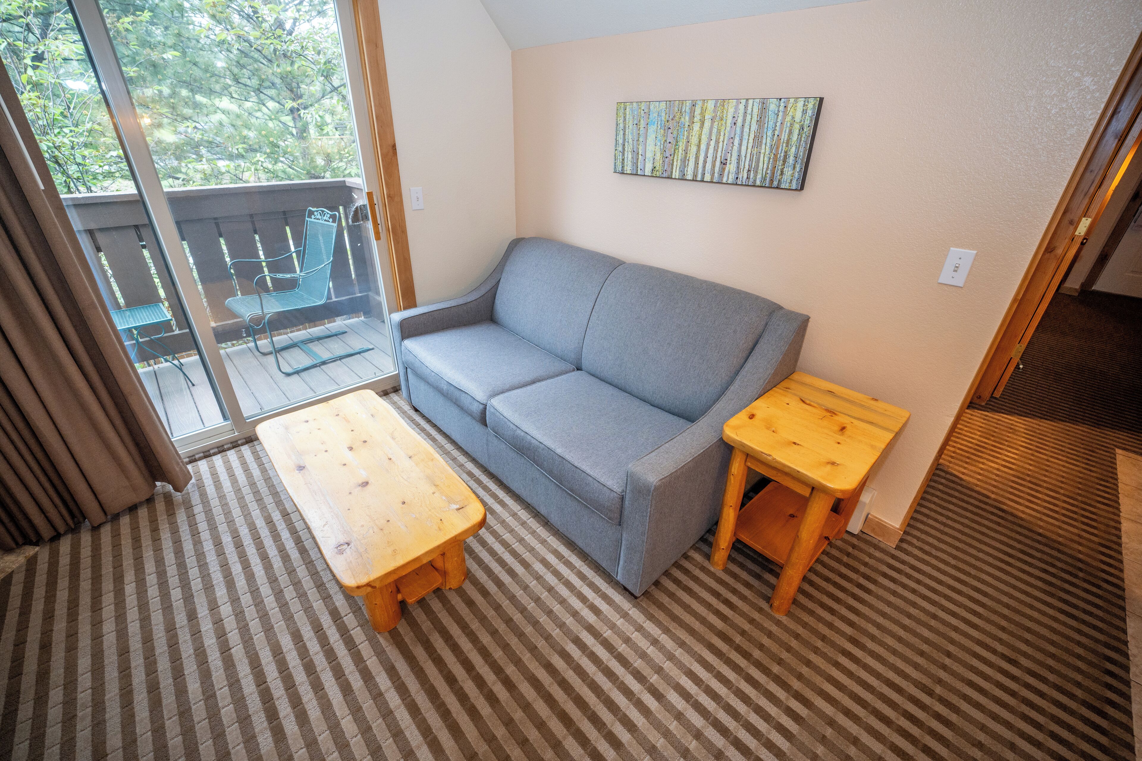 A cozy room with a grey sofa, a wooden table, and a view of greenery outside.