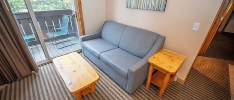 A cozy room with a grey sofa, a wooden table, and a view of greenery outside.