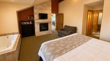 A hotel room with a large bed, a fireplace, a television, and a bathtub.