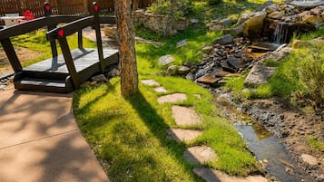 A garden with a wooden bench, a small stream, and a stone wall.