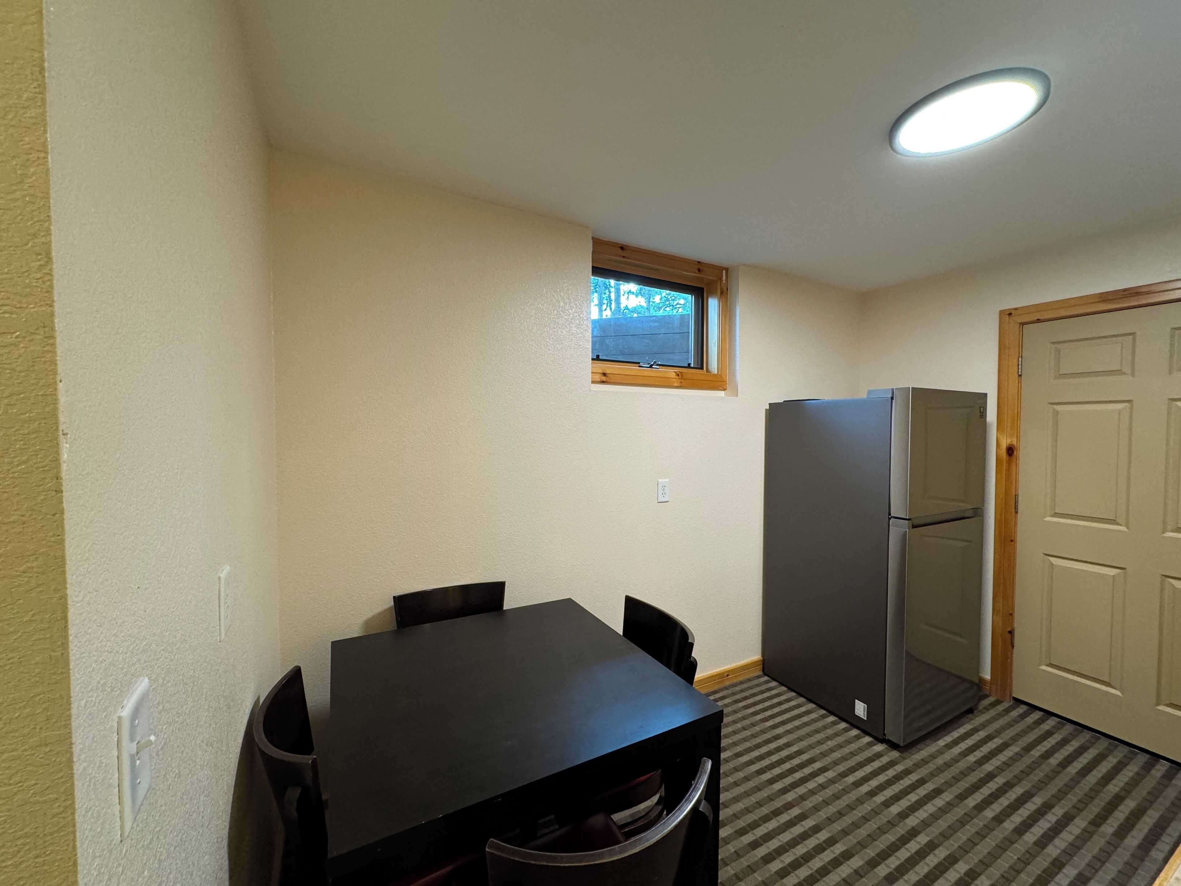 Une petite pièce avec une table et des chaises, un réfrigérateur, une fenêtre et une porte.