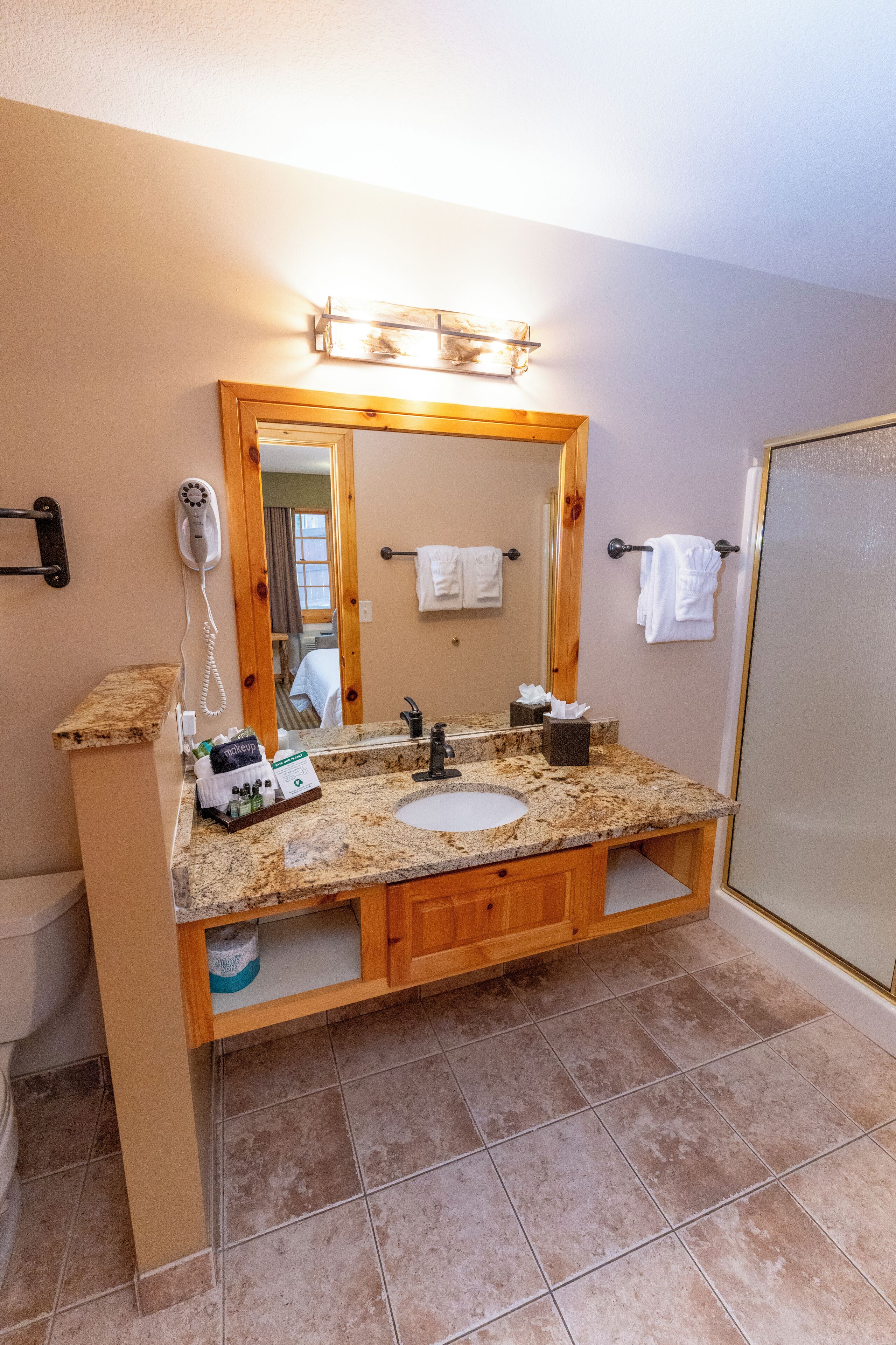 A bathroom with a granite countertop sink, wooden vanity, a large mirror, and a shower enclosure.