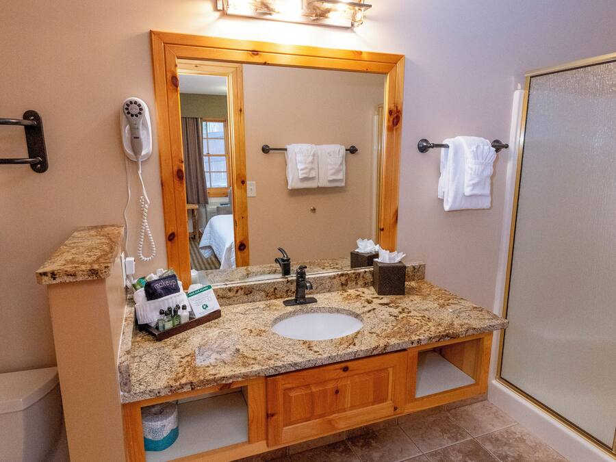 A bathroom with a granite countertop sink, wooden vanity, a large mirror, and a shower enclosure.