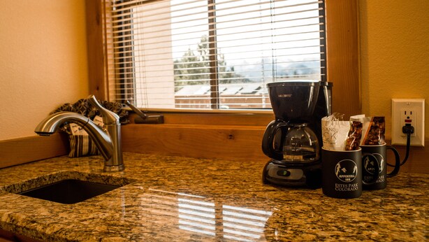 A kitchen counter with a coffee maker, a sink, and a window with blinds.